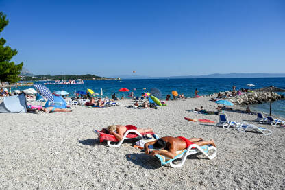 Makarska, Hrvatska: Turisti na plaži i u moru. Makarska, Hrvatska: Turisti na plaži i u moru. Ljetni godišnji odmori. Obala Jadraskog mora ljeti. Turistička sezona. Ljudi se sunčaju i kupaju.