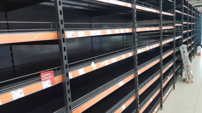 Police bez robe u marketu Prazne police u prodavnici robe široke potrošnje. Police sa cijenama, bez robe. Male ljeste naslonjene na police.