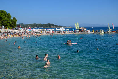 Plaža u Makarskoj puna ljudi Turisti na moru. Ljudi se kupaju i sunčaju u Jadranskom moru. Ljetni odmor. Grupa turista na plaži tokom toplog ljetnog dana. Makarska, Hrvatska.