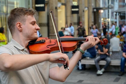 Čovjek svira violinu na gradskom trgu. Ulični svirač svira violinu. Violinista zabavlja publiku na javnom trgu. Ulični nastup.