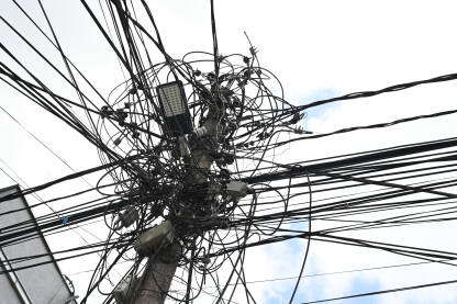 Neuredan snop nadzemnih električnih vodova i komunikacijskih kablova na stubu. Mnogo električnih žica. Bandera  sa mnogo kablova i ulična rasvjeta. Haotične električne žice.