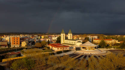 DJI_0604-2 Međugorje tokom zalaska sunca, snimak dronom. Katolička katedrala s dugom i dramatičnim oblacima u pozadini. Religija.
