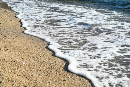 Morska pjena na pješčanoj plaži Morski valovi na pješčanoj plaži tokom zalaska sunca.