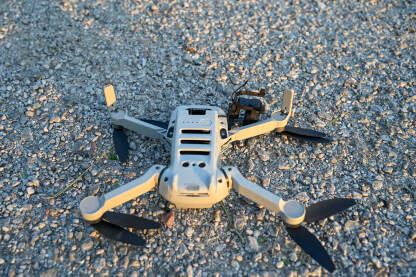Srušen i oštećen dron na asfaltu. Srušen i oštećen dron na asfaltu. Slomljeno kućište i kamera drona. Dron pao na zemlju. Nesreća tokom leta.