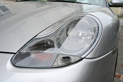 Far automobila, krupni plan. Far automobila, krupni plan. Prednja svjetla sivog automobila na parkingu u gradu. Farovi automobila Porsche.
