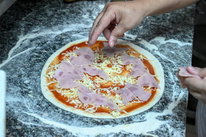 Muškarac priprema pizzu. Priprema ukusne pizze. Muškarac priprema pizzu. Kuhar dodaje salamu na pizzu u kuhinji.