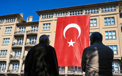 Ljudi ispred ogromne turske zastave na zgradi. Ljudi ispred ogromne turske zastave na zgradi. Nacionalna zastava Turske. Državni i nacionalni simbol. Crvena zastava s bijelom zvijezdom i polumjesecom.