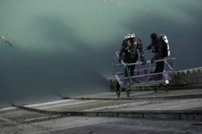 Dva ronioca se spuštaju u korpi, niz betonsku podlogu, do vode u jezeru.