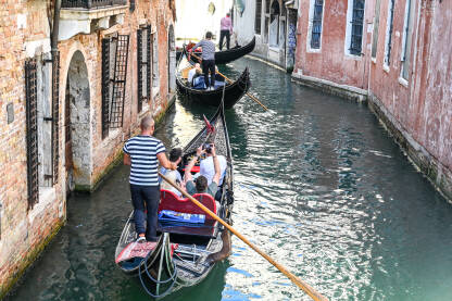 Venecija, Italija: Grupa turista uživa u vožnji gondolom Venecija, Italija: Grupa turista uživa u vožnji gondolom po riječnom kanalu u centru grada. Popularna turistička destinacija. Ljudi sjede u gondoli s gondolijerom.