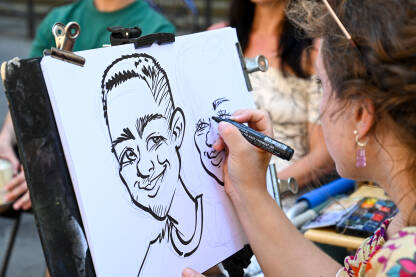 Ulična umjetnost. Žena crta portret para. Ulična umjetnost. Žena crta portret para. Umjetnica crta karikature turista.