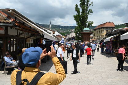 Turist fotografiše stari grad svojim mobilnim telefonima. Grupa turista na Baščaršiji u Sarajevu. Muškarac snima ljude i turističke atrakcije u gradu.