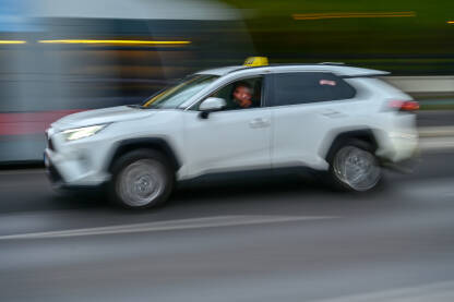 Taksi auto se brzo kreće cestom u gradu. Prijevoz. Bijeli auto u gradu, zamućena fotografija. Taxi.