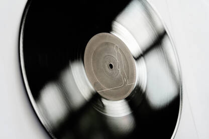 Gramofonska ploča Ova slika prikazuje crno-belu vinilnu gramofonsku ploču na beloj pozadini. Ploča djeluje izgrebano i istrošeno, s brazdama koje su vidljive, na beloj pozadinom koja je u kontrastu s crno-belom pločom.