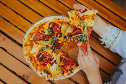 Pizza na stolu Pizza na drvenom stolu, djevojka uzima komad pizze