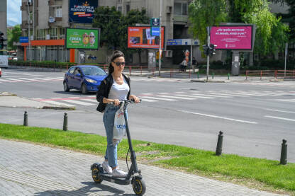Žena vozi električni trotinet Žena vozi električni romobil u gradu. Prijevoz u gradu. Mlada žena vozi romobil.