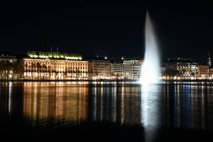 Hamburg, Njemačka. Zgrade u centru grada noću. Hamburg, Njemačka. Toranj gradske vijećnice, zgrade i Alster jezera noću. Cityscape. Refleksija svjetla u vodi.