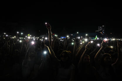 Ljudi drže mobilne telefone Ljudi drže mobilne telefone i upaljače na koncertu. Obožavatelji koriste svjetla pametnog telefona na muzičkom festivalu. Ljudi na koncertu su upali mobilne telefone na rock koncertu.