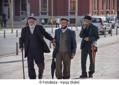 Stariji ljudi nose maske Stariji muškarci hodaju ulicom sa maskama na bradi. Trojica starijih muškaraca hodaju ulicom tokom pandemije virusa korona u Draču, Albanija.