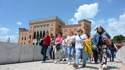 Grupa turista u Sarajevu Sarajevo, Bosna i Hercegovina: Grupa turista u gradu. Ljudi istražuju grad. Turisti na mostu sa gradskom vijećnicom u pozadini.
