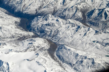 Let iznad planina prekrivenih snijegom. Pogled kroz prozor aviona na bijele planinske vrhove. Alpe u Austriji.