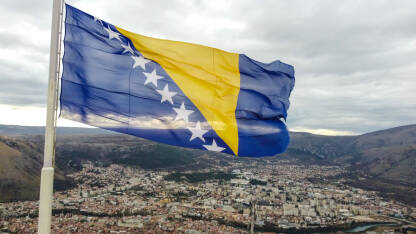 Državna zastava Bosne i Hercegovine. Zastava BiH. Državna zastava Bosne i Hercegovine se vijori na vjetru. Nacionalna zastava Bosne i Hercegovine na jarbol iznad grada Mostara, snimak dronom.