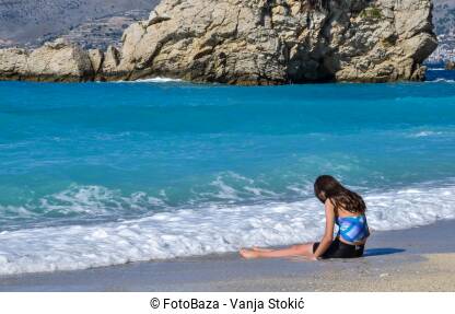 Djevojka na plaži Lijep, sunčan dan na plaži u Ksamilu, Albanija. Djevojka sjedi sama na plaži. Tužna djevojka sjedi na obali mora.