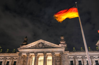 Njemačka državna zastava se vijori u Berlinu, Njemačka. Njemačka državna zastava se vijori na jarbolu ispred zgrade Reichstaga u Berlinu, Njemačka. Državni i nacionalni simbol. Njemački Bundestag.