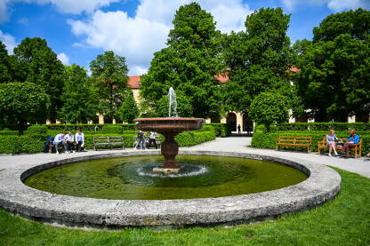 Fontana sa vodom u parku. Ljudi sjede na klupama u parku blizu fontane. Osvježenje tokom toplih ljetnih dana.