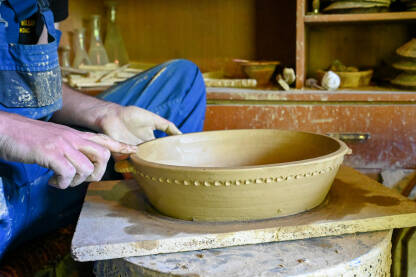 Majstor radi s glinom na grnčarskom kolu. Čovjek obrađuje glinu. Majstor pravi glinenu zdjelu. Obrada gline. Proizvodnja keramičkog posuđa od prirodnih materijala.