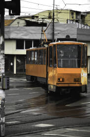 Zuti tramvaj koji skrece Tramvaj u voznji, koji se krece levo, stambene zgrade u pozadini, tmuran dan bez sunca.