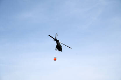 Helikopter u akciji Helikopter u akciji gašenja požara u šumi. Helikopter leti sa kantom za vodu.