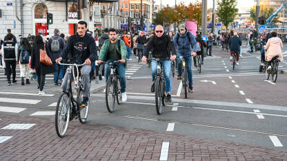 Grupa ljudi vozi bicikle u Amsterdamu Amsterdam, Nizozemska: Grupa biciklista vozi bicikle po ulici. Biciklizam u gradu. Ljudi koriste bicikle za vožnju.
