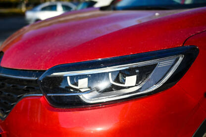 Far automobila, detalj. Prednja svjetla crvenog automobila na parkingu u gradu.