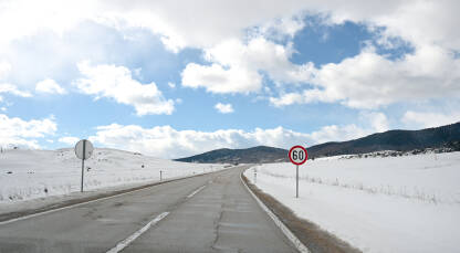 Ograničenje brzine 60 km/h Snježni put zimi. Saobraćajni znak uz asfaltni put u prirodi.