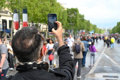 Muškarac snima ljude na ulici mobilnim telefonom Muškarac mobilnim telefonom snima ljude na ulici. Čovjek snima pametnim telefonom ljude u gradu Parizu. Turist sa mobilnim telefonom snima fotografije.