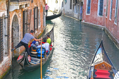 Venecija, Italija: Grupa turista uživa u vožnji gondolom Venecija, Italija: Grupa turista uživa u vožnji gondolom po riječnom kanalu u centru grada. Popularna turistička destinacija. Ljudi sjede u gondoli s gondolijerom.