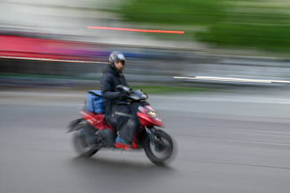 Čovjek se brzo kreće na skuteru na ulici. Čovjek se brzo kreće na motociklu na ulici. Vožnja skuterom po gradu. Vozač motocikla. Blurana fotografija.