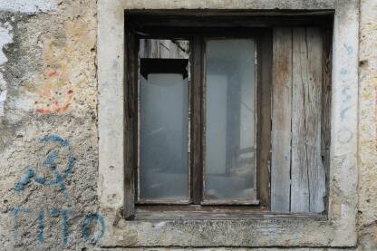 Dio fasade napuštenog objekta sa polomljenim prozorom i plavim natpisom Tito, znakom srpa i čekića