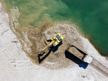 DJI_01411 Bager kopa i utovaruje pijesak u kamion na obali rijeke. Teški strojevi rade u kamenolomu pijeska. Snimak dronom na bager i kamion koji utovaruju šljunak u prirodi. Zagađenje okoliša i vode