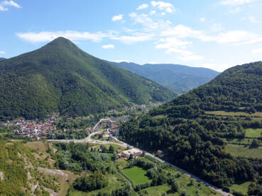 Opština Jezero. Naselje u dolini. Visoko brdo sa šumom iznad sela. Naselje u dolini, snimljeno dronom. Jezero, Bosna i Hercegovina.
