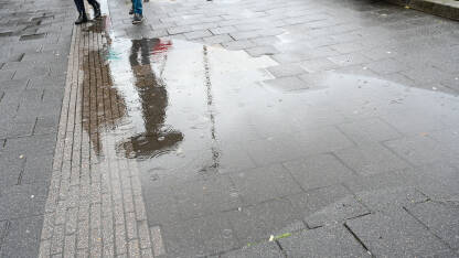 Refleksija osobe sa kišobranom u lokvi vode. Refleksija osobe sa kišobranom u lokvi vode. Kiša na asfaltnom putu. Kapljice kiše u lokvi. Ljudi sa hodaju sa kišobranom.