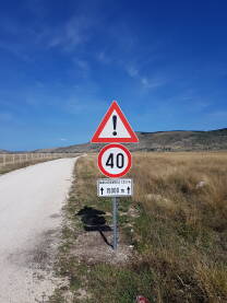 Saobraćajni znakovi, makadamska cesta Saobraćajni znakovi koji označavaju ograničenje brzine kretanja vozila na 40 km/h i opreznu vožnju zbog kretanja po makadamskoj cesti u dužini od 15.000 m, tj. 15 km