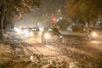 Automobili se kreću po cesti po zimskoj mećavi. Obilni snijeg u gradu noću. Jake snježne padavine ometaju saobraćaj u gradu. Noćni gradski saobraćaj.