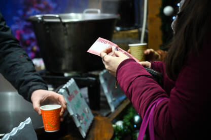 Žena plaća piće novčanicom na pijaci ili uličnom štandu. Žena kupuje šolju vrućeg kuhanog vina. Plaćanje forintama u Mađarskoj.