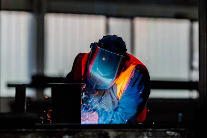 Zavarivač radi na metalnoj konstrukciji u industrijskoj radionici, sa varnicama i zaštitnom opremom