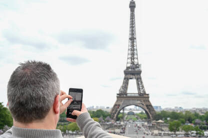 Turista u Parizu, Ajfelov toranj Pariz, Francuska: Turisti fotografišu Eiffelov toranj. Muškarac fotografiše Pariz svojim pametnim telefonom. Popularna turistička destinacija.