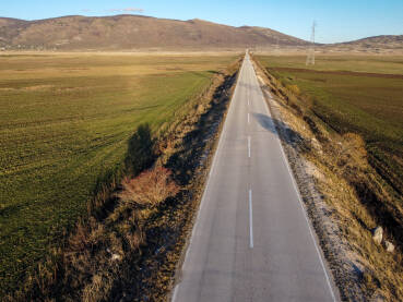 DJI_0545 Snimak dronom na dugu ravnu cestu u polju. Asfaltna cesta u polju tokom zalaska sunca. Seoski krajolik s ravnom cestom. Kupreško polje, Kupres, Bosna i Hercegovina.