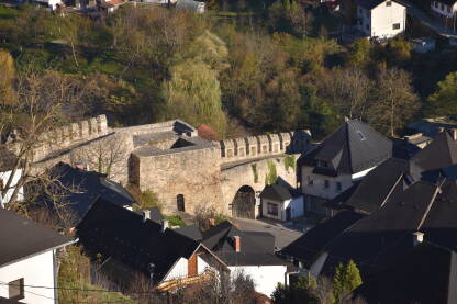 Banjalučka kapija u Jajcu Banjalučka kapija u Jajcu u fokusu pored drugih stambenih gradskih objekata i vidljive zelene površine.