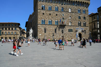 Firenca, Italija: Palazzo Vecchio, replika kipa Davida i Neptunova fontana na Piazza della Signoria. Firenca, Italija: Palazzo Vecchio, replika kipa Davida i Neptunova fontana na Piazza della Signoria. Ljudi šetaju trgom. Historijske građevine. Turisti istražuju grad.