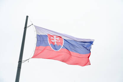 Zastava Slovačke se vijori na vjetru Zastava Slovačke se vijori na vjetru ispred parlamenta. Zastava Slovačke na jarbolu. Bijela, plava i crvena boja. Državni grb Slovačke.